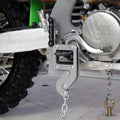 TurnLock Moto Peg Binder clamped on a dirt bike footpeg, chained to a tie-down point